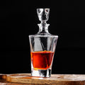 Clear glass decanter with red liquid on a wooden surface against a black background