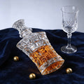 Decorative glass decanter with amber liquid next to a clear glass on a dark blue fabric background.