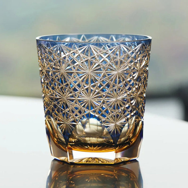 Decorative glass tumbler with intricate cut patterns on a reflective surface.