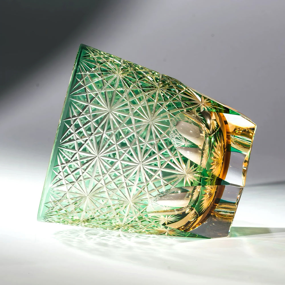 Decorative glass tumbler with intricate cut patterns on a reflective surface.