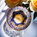 Decorative glass with blue and gold floral design on a white surface with yellow roses.