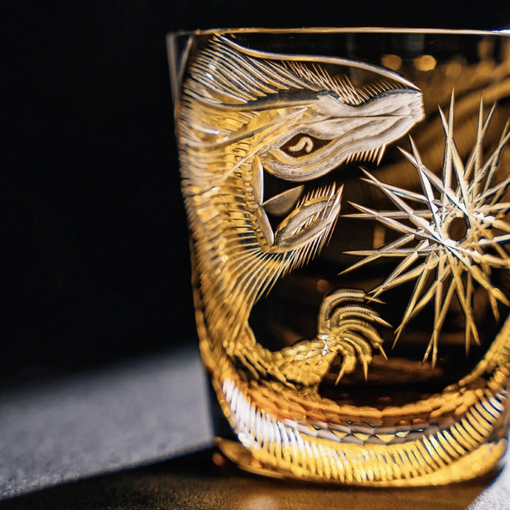 Decorative glass with intricate gold engravings of a dragon and floral design on a dark background