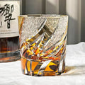Decorative glass with intricate designs filled with amber liquid, next to a bottle of whiskey.