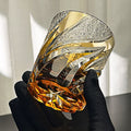 Hand holding a large, faceted crystal with gold and silver accents against a neutral background