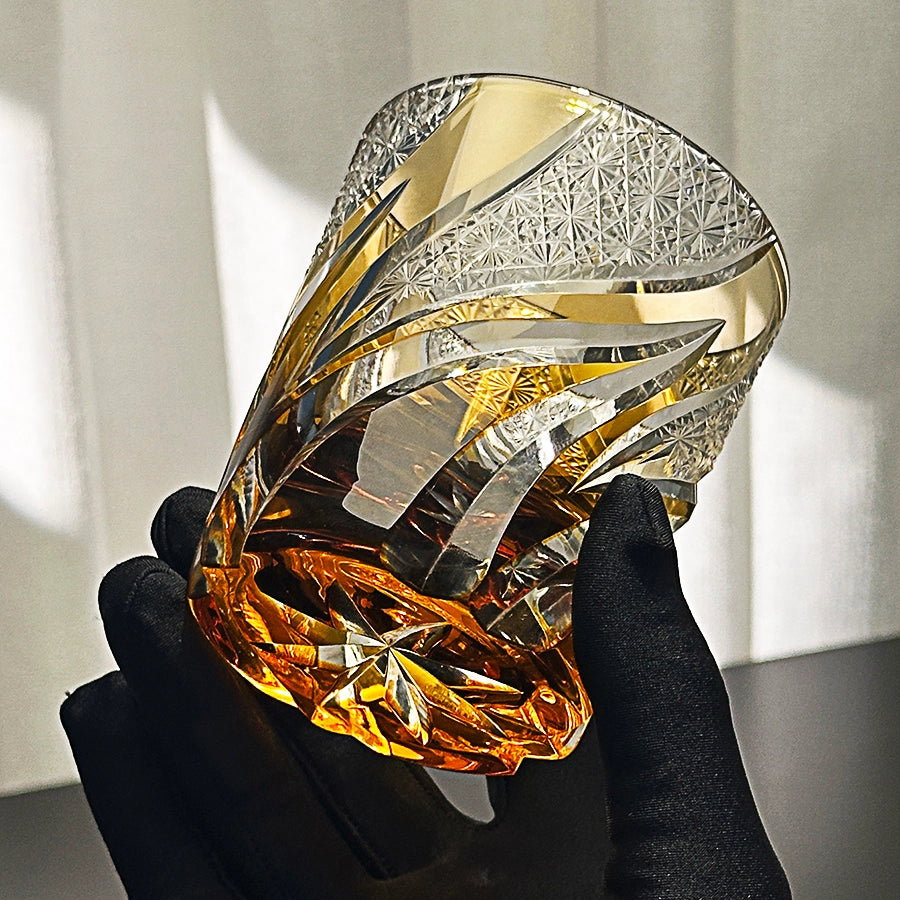 Hand holding a large, faceted crystal with gold and silver accents against a neutral background