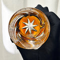 Glass with star design filled with amber liquid held by a black glove against a neutral background