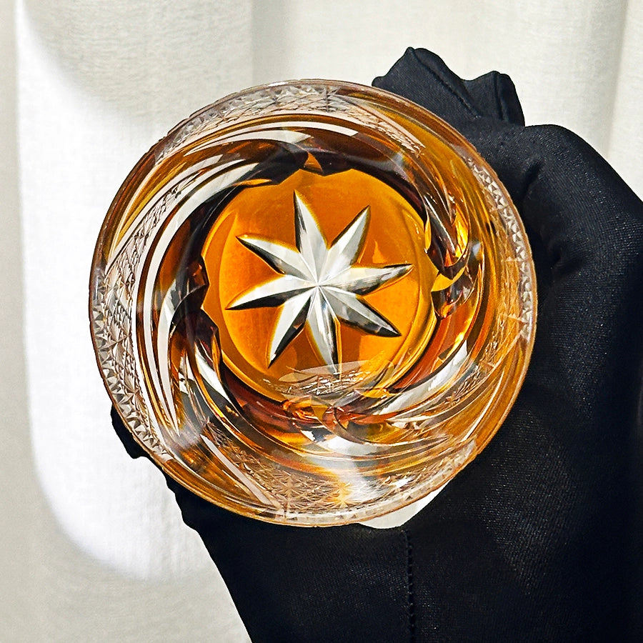 Glass with star design filled with amber liquid held by a black glove against a neutral background
