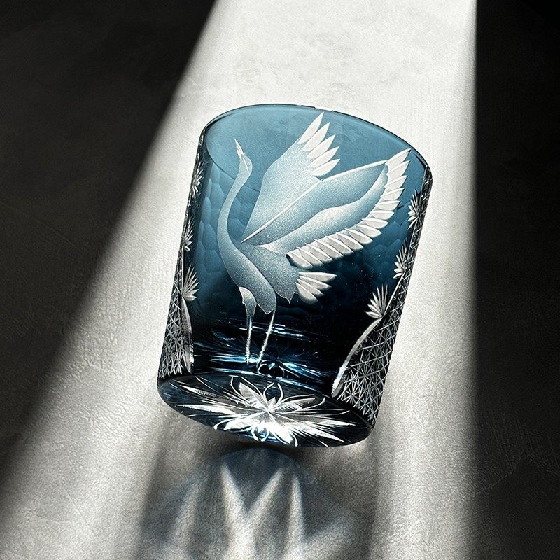 Decorative glass with engraved crane design on a light fabric background