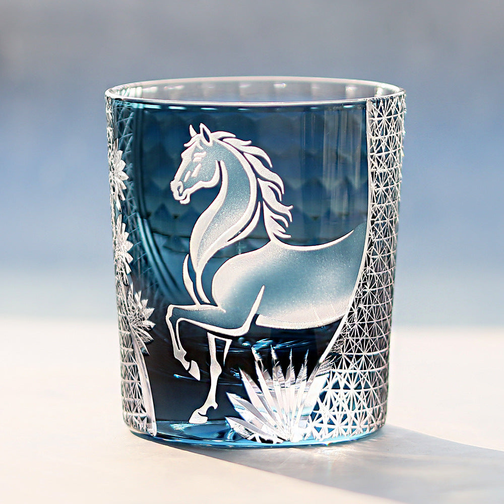 Blue glass tumbler with horse etching on a light gray background