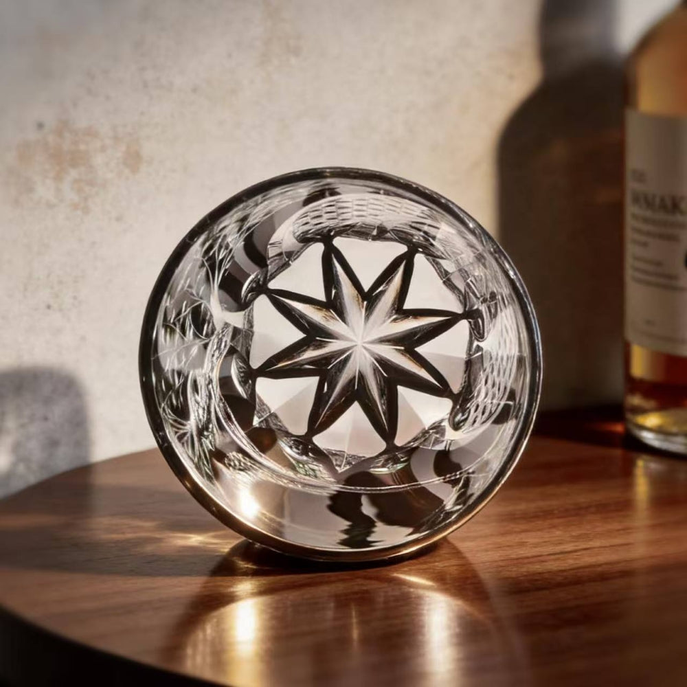 Crystal glass with star design on a wooden surface, with a bottle in the background.