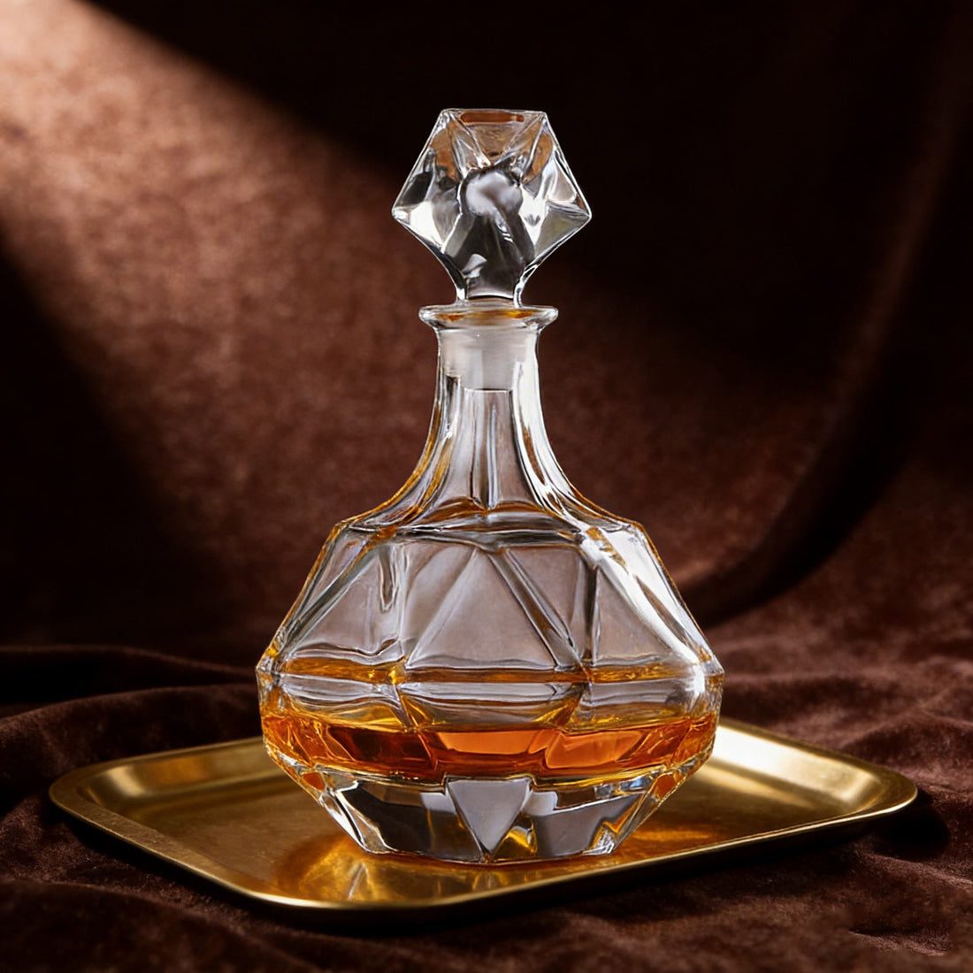 Glass decanter with a diamond-shaped stopper on a gold tray against a brown background