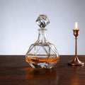 Glass whiskey decanter with a candle on a wooden surface
