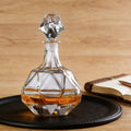 Clear glass decanter with geometric design on a wooden surface with an open book and pen.