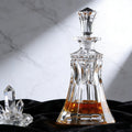 Clear glass decanter with liquid on a black surface and marble background